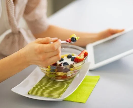 Closeup on young woman eating fruits salad and using tablet pc