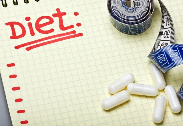 notebook with diet plan and a measuring tape with pills